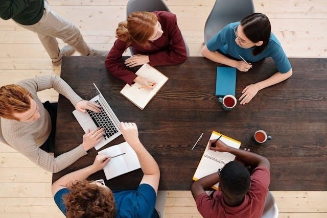 An aerial view of a group of people sitting around a table with notebooks and a laptop